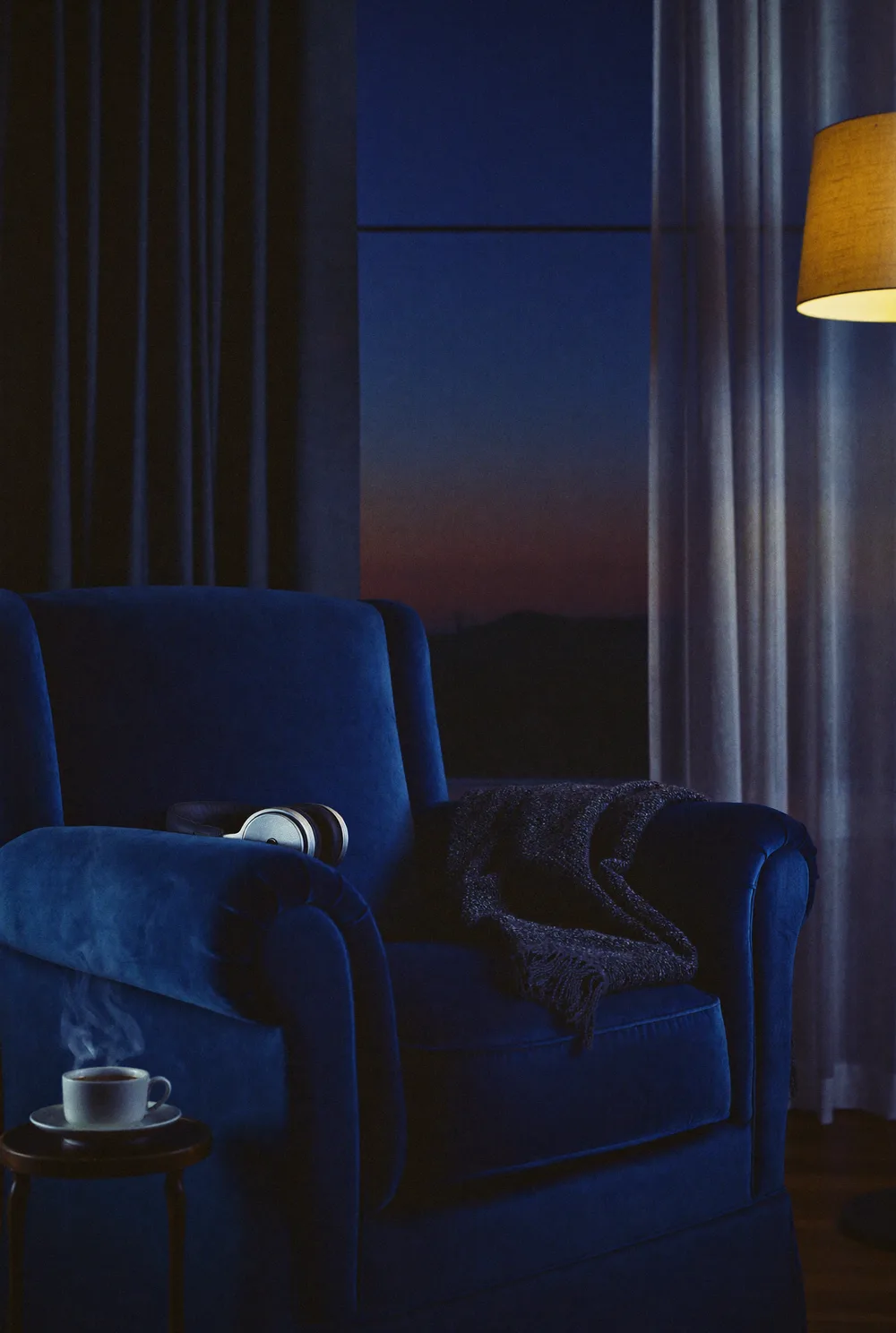 A velvet armchair at dusk with headphones and tea